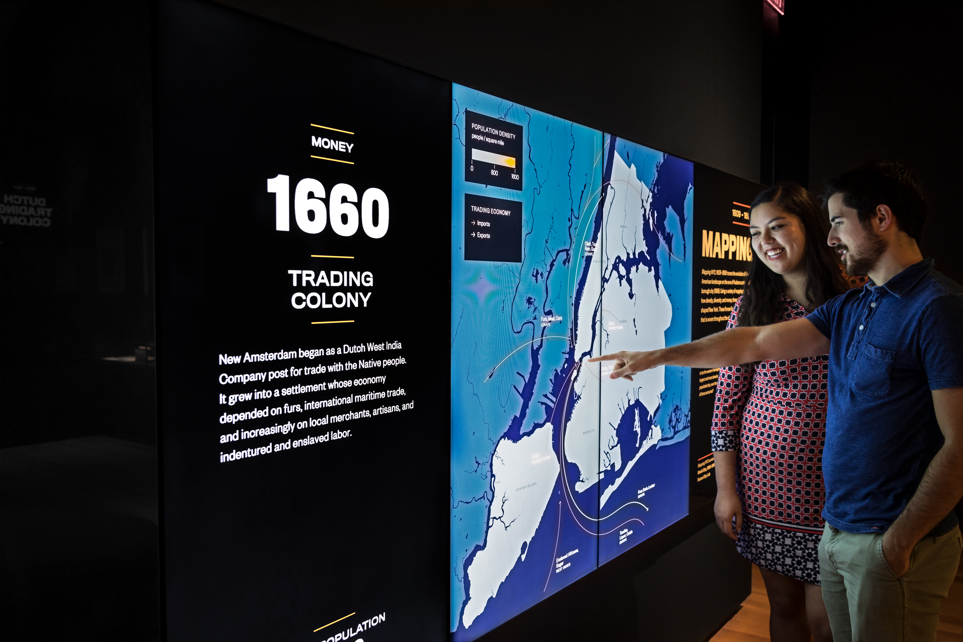 Two visitors point out details on a screen in an exhibition space