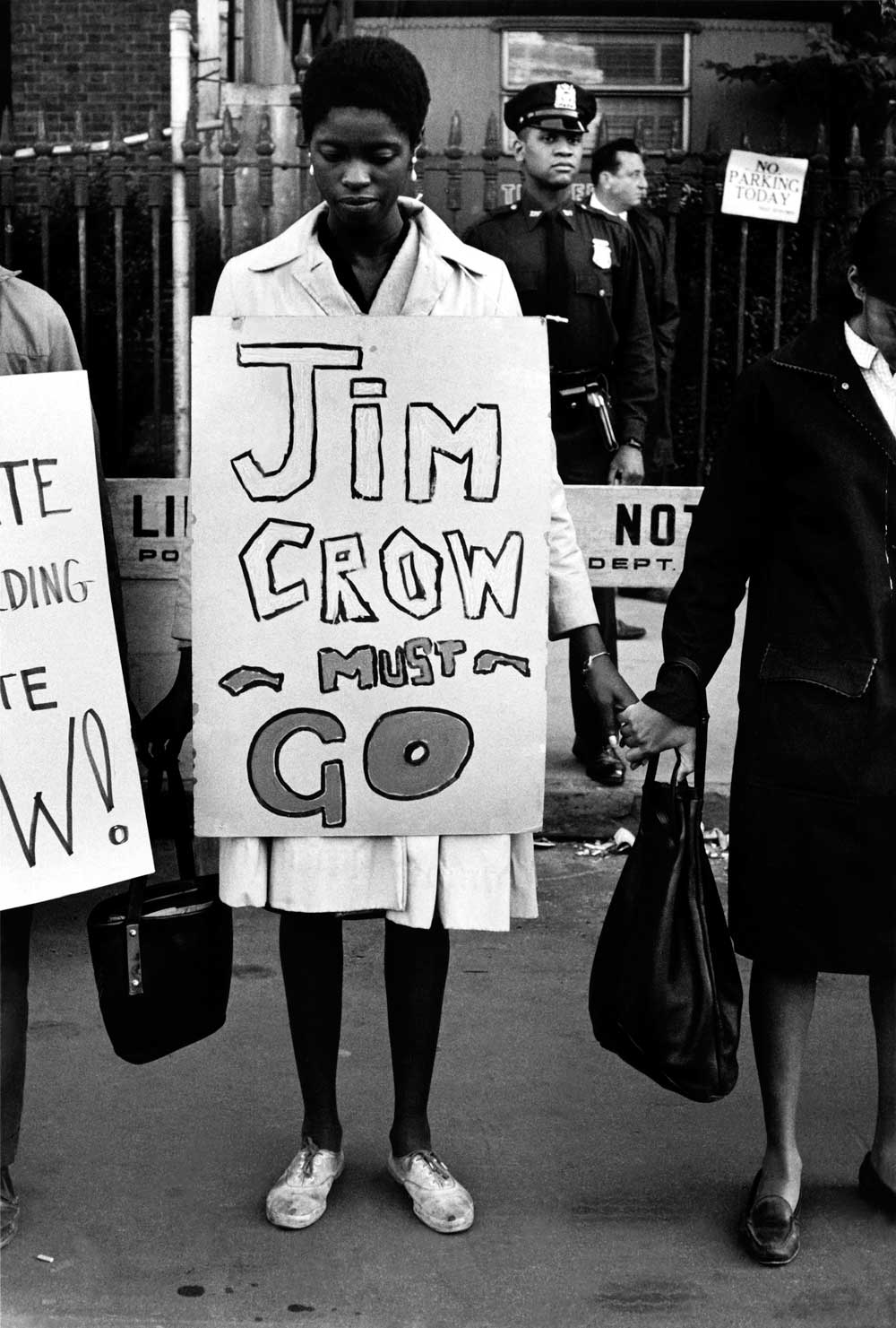 Uma mulher está de pé em uma fila de manifestantes de mãos dadas, com uma placa ao redor dizendo "Jim Crow deve ir"