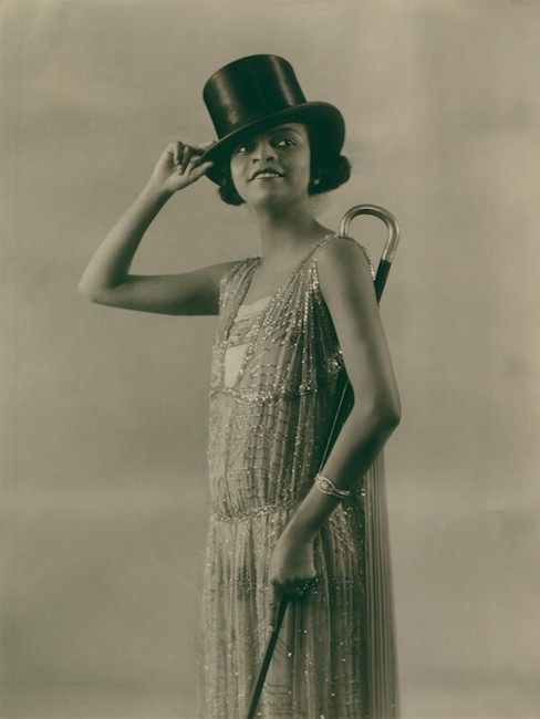 Una fotografía en blanco y negro de Florence Mills posada en un elegante vestido con sombrero de copa y bastón
