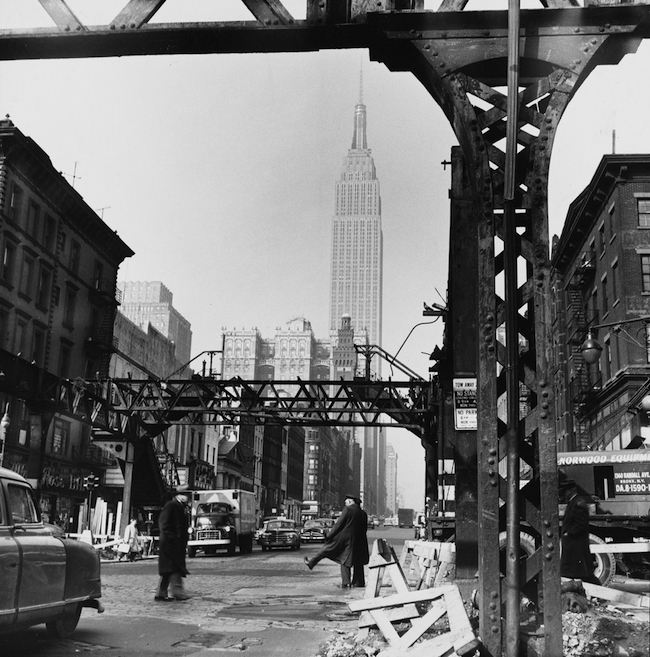 Fotografia de trilhos de trem elevados parcialmente desmontados com o Empire State Building em segundo plano.