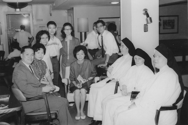 Photo en noir et blanc d'une famille asiatique assise avec un groupe de religieuses.