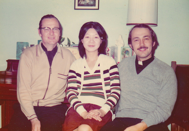 Fotografía en color de los Padres Denis Hanly (derecha) Joanna Chan y Richard Grillo (izquierda), sentados en una sala de estar.