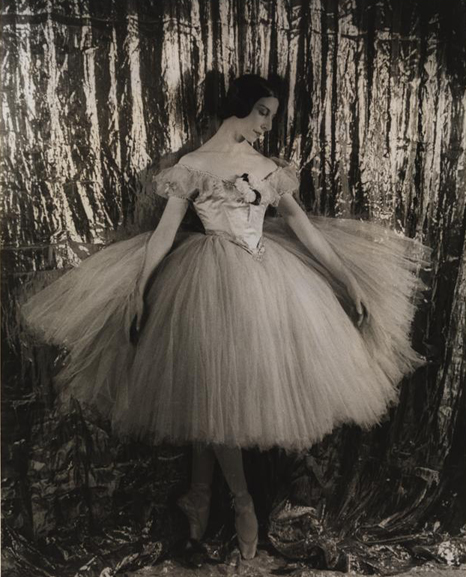 Un retrato de una bailarina, en traje, de pie en punta delante de una cortina.