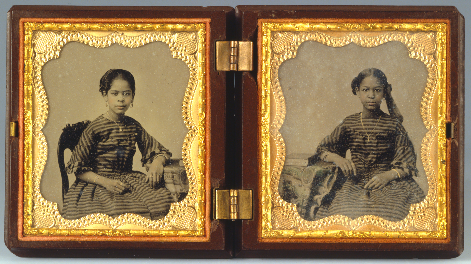 Two black and white photographs on each side of a hinged wood and gold case show two Black girls wearing dresses in matching fabric and jewelry.