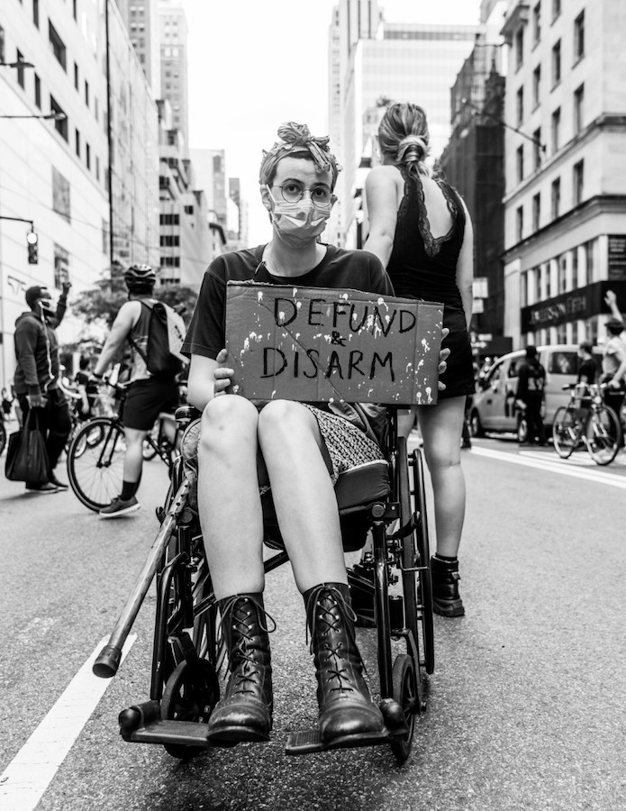車いすの女性が抗議の看板を掲げている。