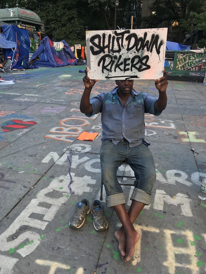 Manifestante com placa de "Desligue Rikers" na prefeitura de ocupação.