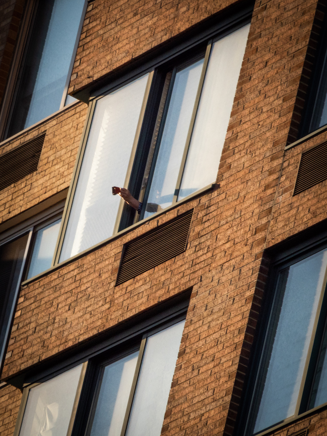 COVID-7のパンデミックの間、誰かが「午後19時の敬礼」の一環としてアパートの窓の外で鳴子を持っています。
