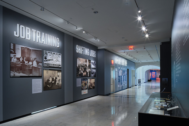 Vista de instalación de "Ciudad analógica: Nueva York BC (antes de las computadoras)", que muestra imágenes y texto en las paredes junto con otros objetos