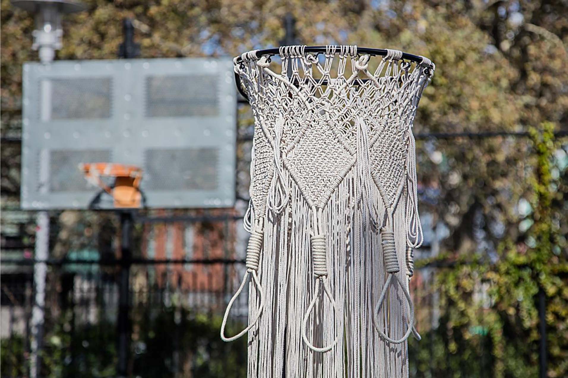 Photographie du bord d'un panier de basket-ball avec un filet en macramé suspendu.