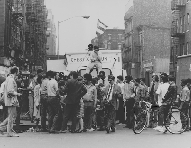 Young Lords의 일원이 East Harlem 거주자에게 무료 결핵 검사를 제공하기 위해 캠페인을 진행하는 동안 흉부 -X 레이 유닛 트럭 위에 앉아 있습니다.