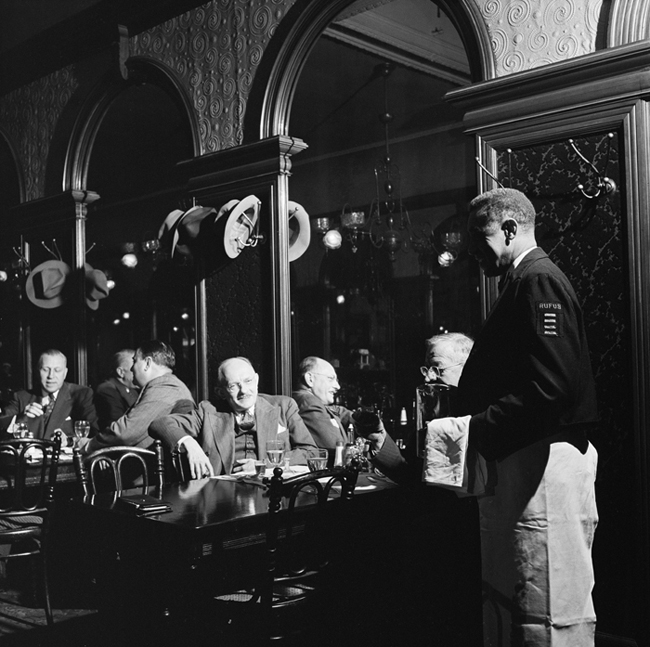 Interior of Gage and Tollner restaurant with men eating and waiter nearby.
