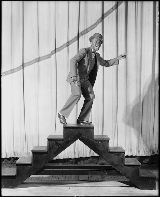 Bill "Bojangles" Robinson se para en un conjunto de escaleras frente a una cortina como parte de la producción "Blackbirds".