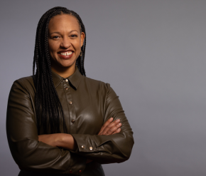 Woman smiling with her arms crossed in front of a grey backdrop