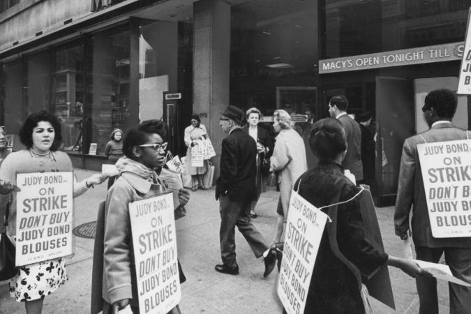 Um grupo de trabalhadores em greve marcham do lado de fora da Macy's enquanto usam cartazes incentivando as pessoas a não comprar blusas de Judy Bond