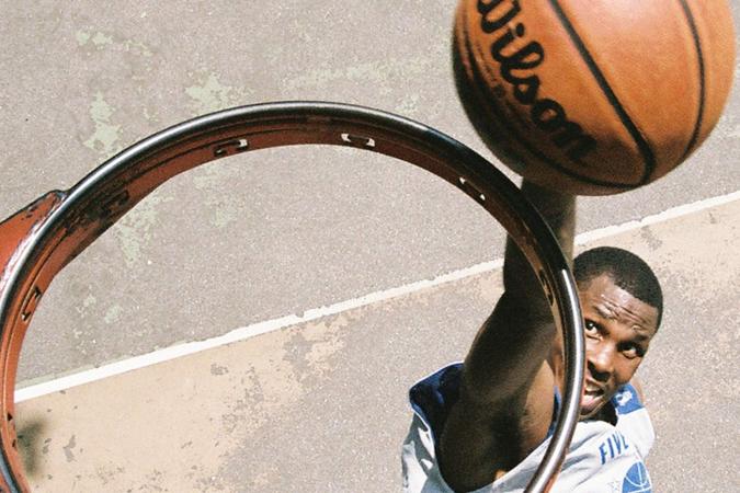 Vista de cima de uma cesta de basquete sem rede, onde um jogador é visto prestes a enterrar uma bola de basquete no aro