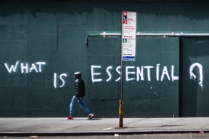 Um homem passa por uma parede fechada com tábuas com as palavras "O que é essencial" pintadas em spray.