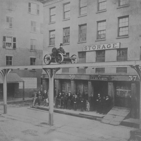 Photo en noir et blanc d'un homme monté sur un chariot sur une plate-forme surélevée au-dessus d'une rue de la ville.