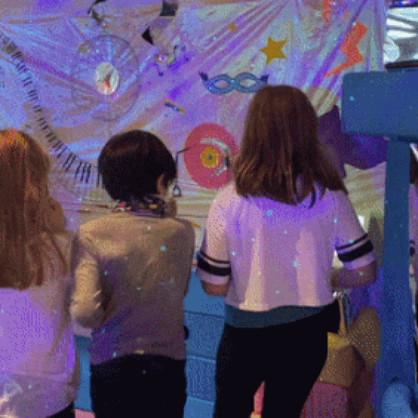 Quatre enfants se tiennent devant un présentoir coloré.