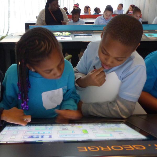 Tres estudiantes de primaria se reunieron alrededor de una pantalla de tableta en el museo, aprendiendo digitalmente