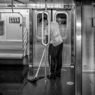 A man with a mop cleans the floor of a subway car in front of a subway door.