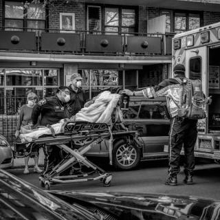 A person on a stretcher is being wheeled into an ambulance assisted by three medical workers. A fourth person stands nearby.