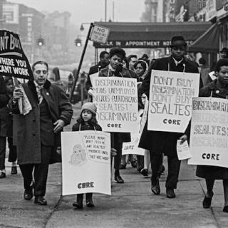 A black and white photograph of people from Brooklyn CORE walking with signs in a boycott against Sealtest Dairy Company in 1963.