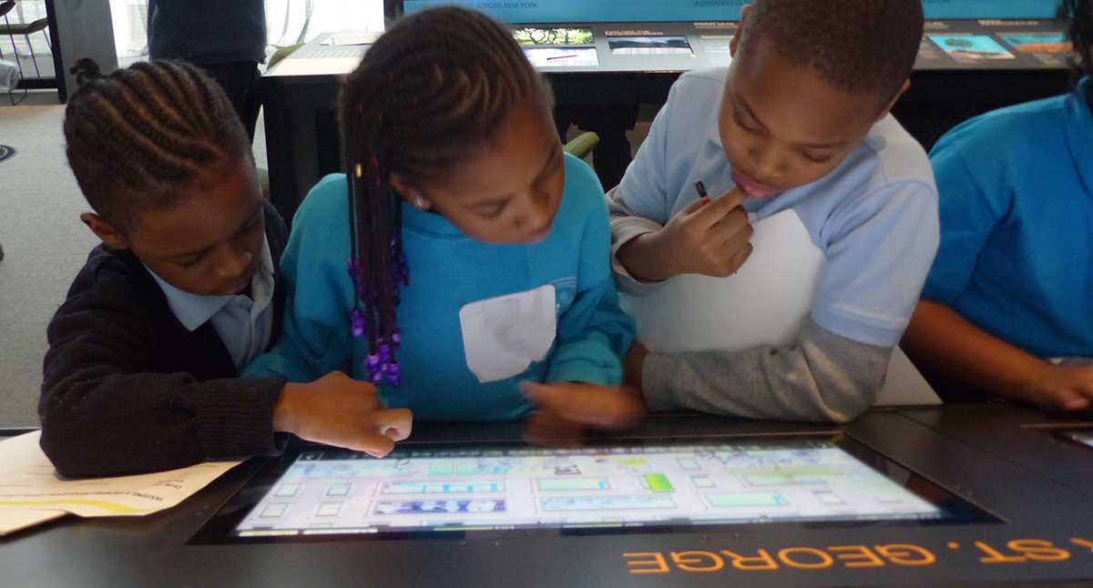 三个小学生聚集在博物馆的平板电脑屏幕上，进行数字学习
