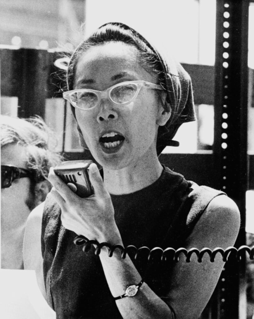 A woman in glasses and a bandana speaks into a radio. 