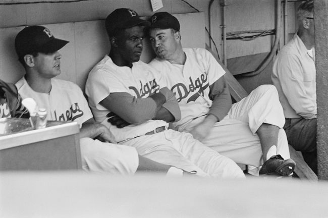 Jackie Robinson tiene una conversación con su compañero de equipo Duke Snider en el banquillo durante un partido de béisbol