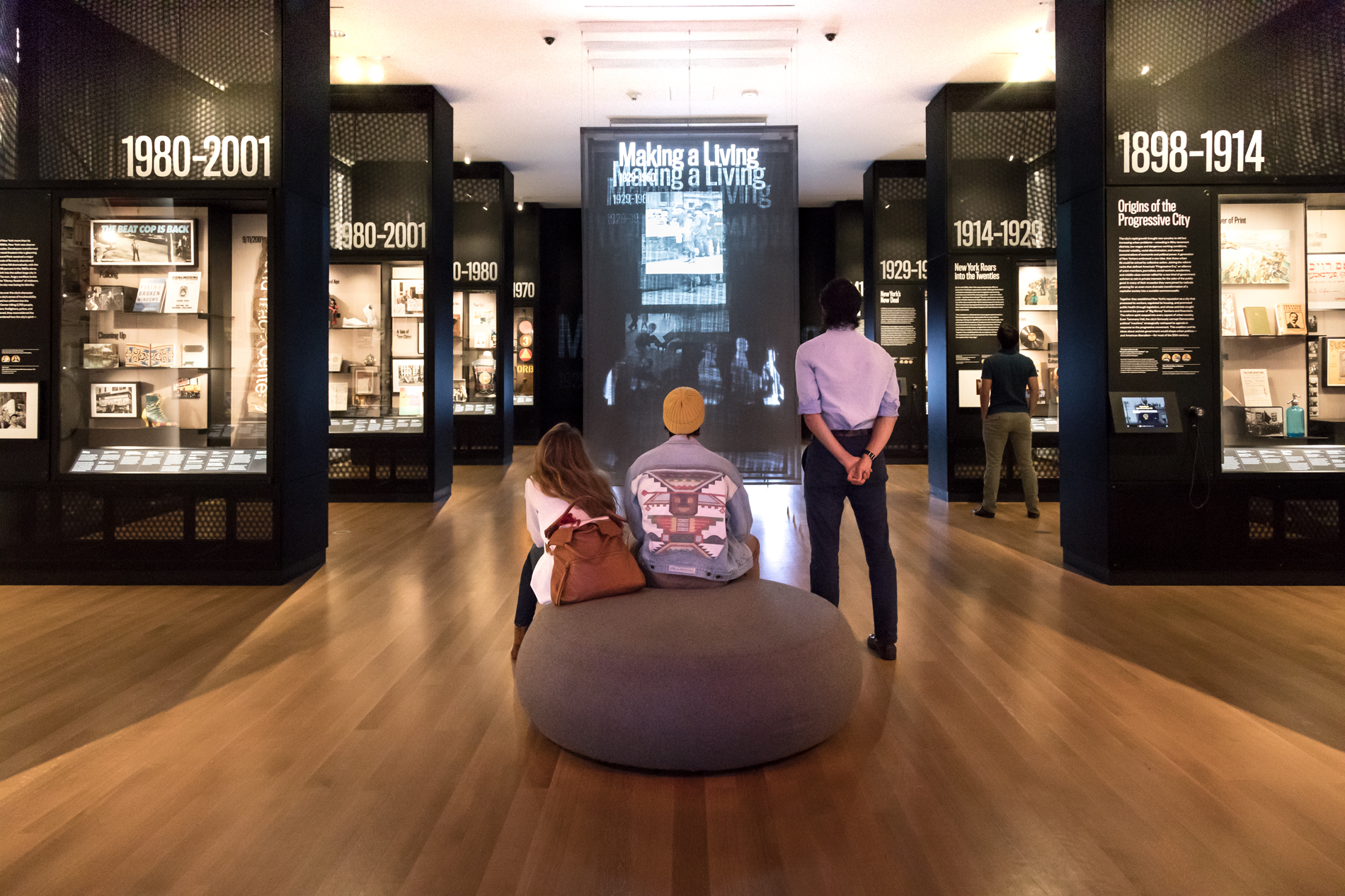 Visitors sit and stand while looking at a video display in a gallery