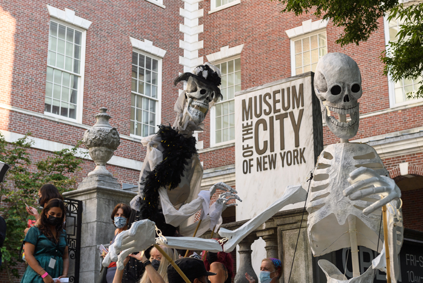 Dos grandes marionetas de esqueletos están uno frente al otro. Hay un cartel con las palabras “Museo de la Ciudad de Nueva York” detrás de ellos.