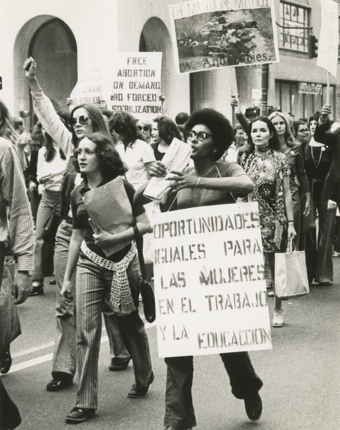 A group of women march in a rally, many are holding protest signs