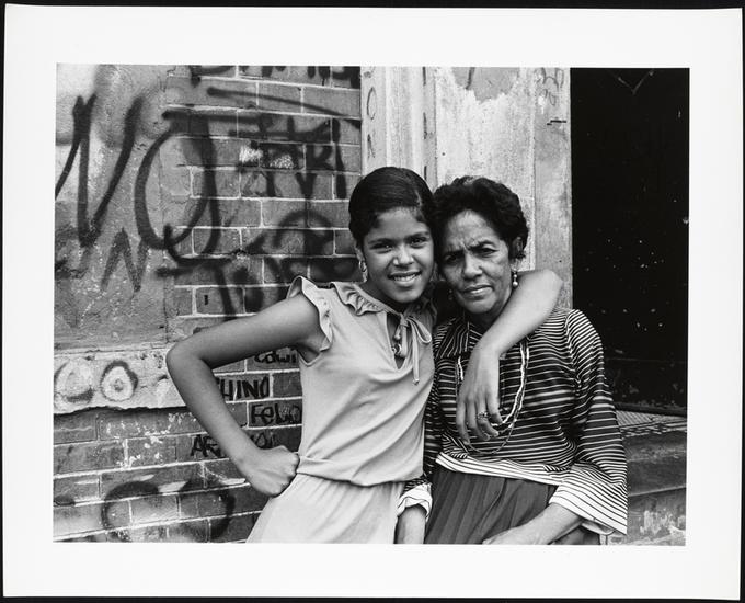 Two women pose in front of a graffitied building in the South Bronx of New York City