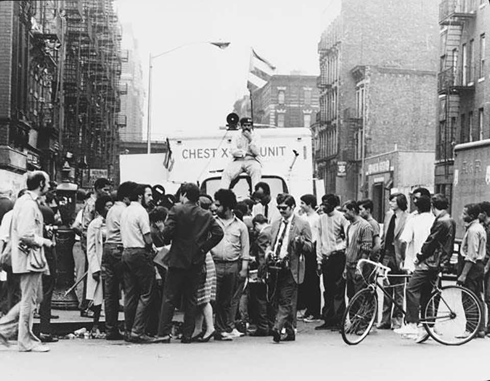 A group of young activists and journalists stand in front of a mobile x-ray truck, which is flying a Puerto Rican flag. 