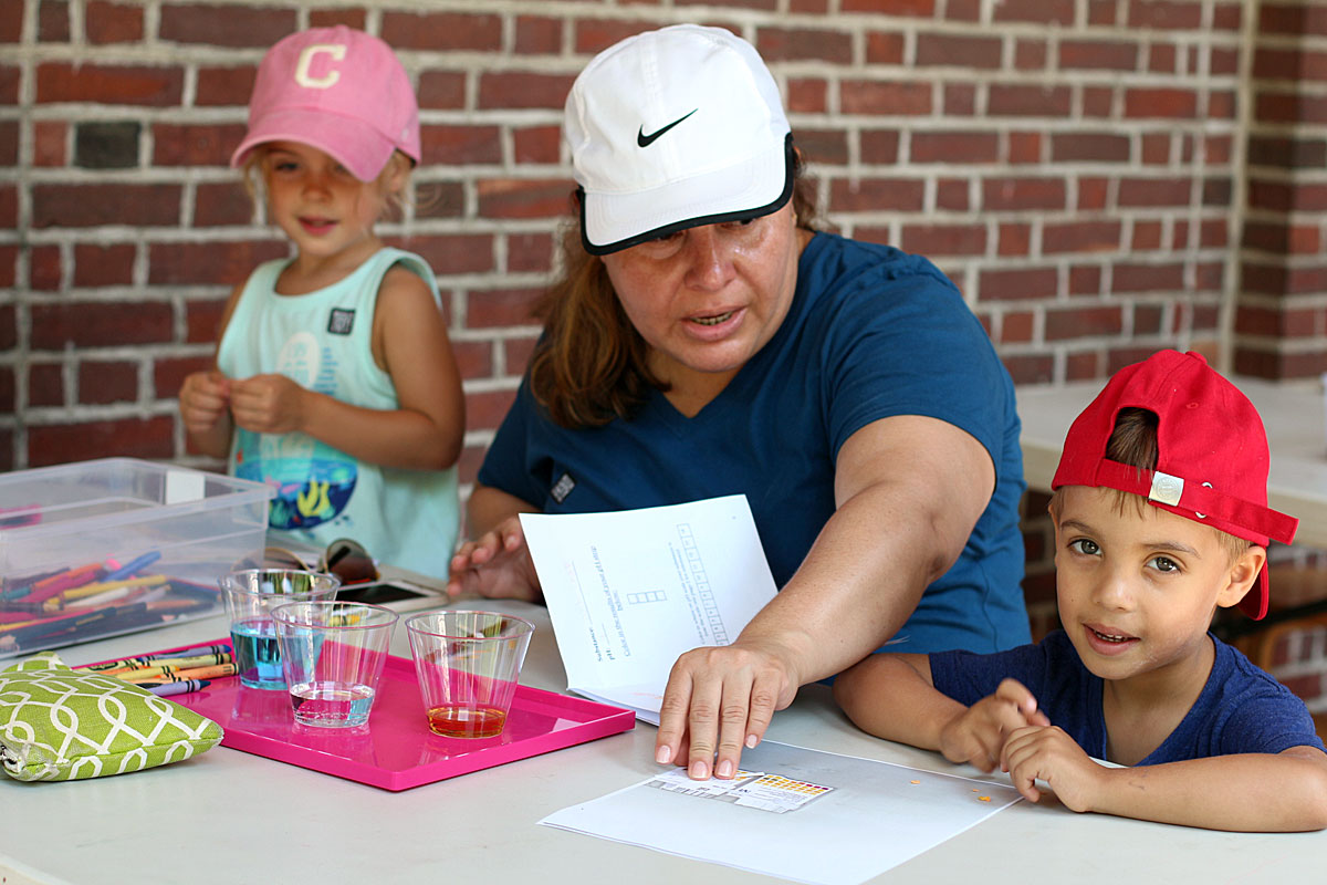 Photograph of a family participating in a wet water lab, involving the testing varying pH levels of different liquids. 