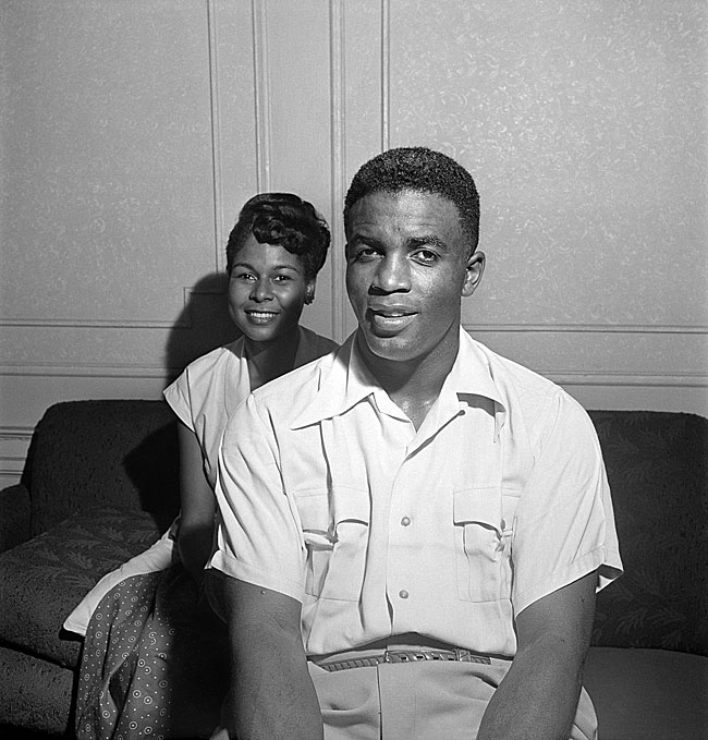 Photographie en noir et blanc du magazine Look montrant Jackie et Rachel Robinson dans leur maison. Le couple est assis sur un canapé à l'intérieur de leur appartement.