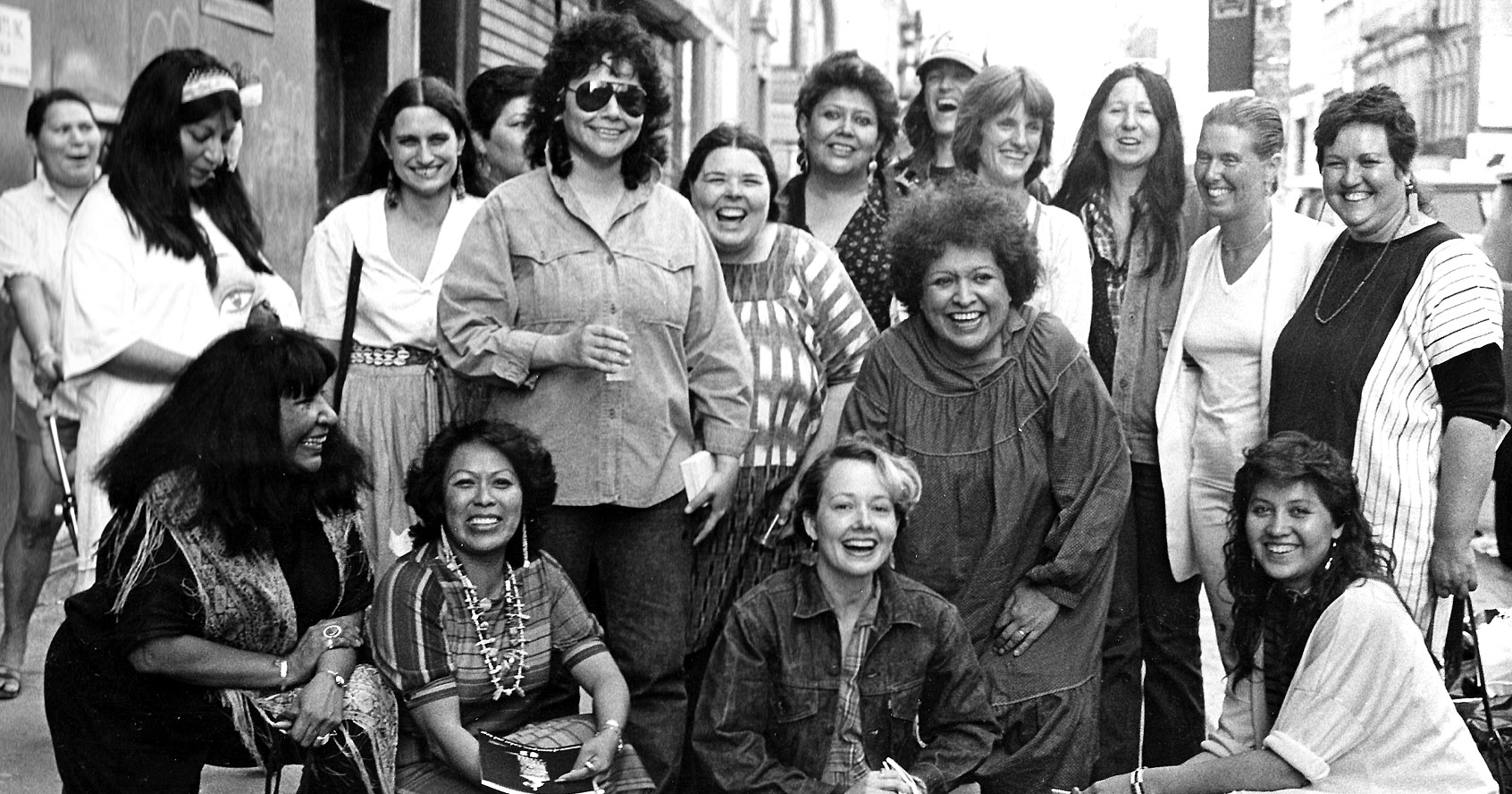 Photograph of artists from the exhibition, Women of Sweetgrass, Cedar and Sage, friends and community members outside the American Indian Community House Gallery taken in 1985. 