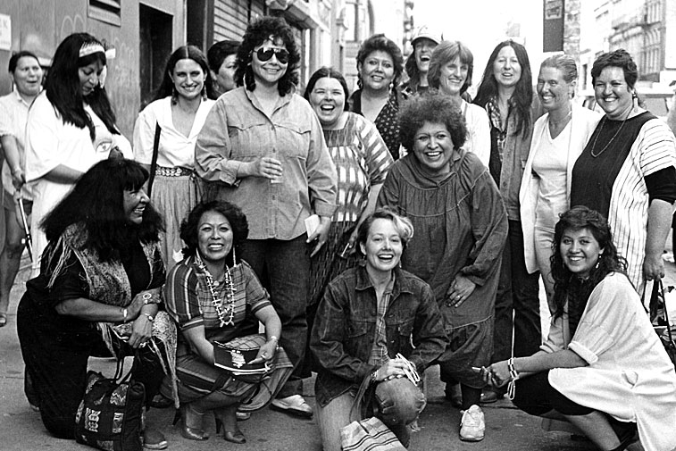 Photograph of artists from the exhibition, Women of Sweetgrass, Cedar and Sage, friends and community members outside the American Indian Community House Gallery taken in 1985. 