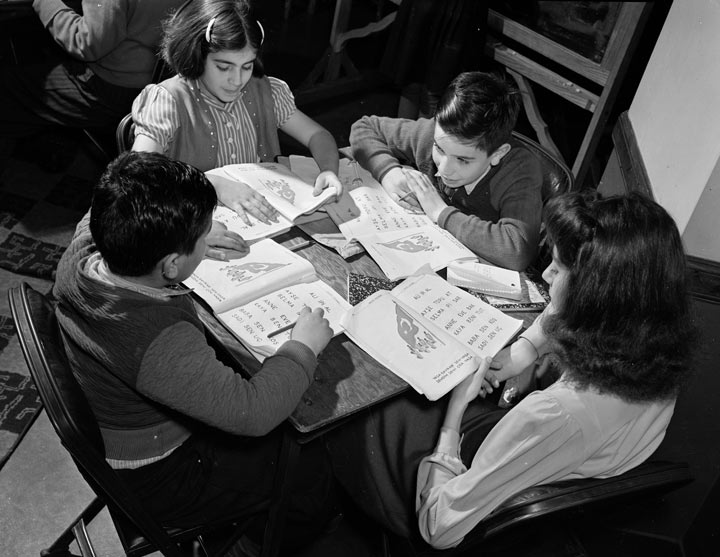 Quatro crianças sentam-se ao redor de uma mesa olhando os livros na frente deles