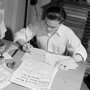 一个男人坐在一张被报纸包围的桌子旁的照片