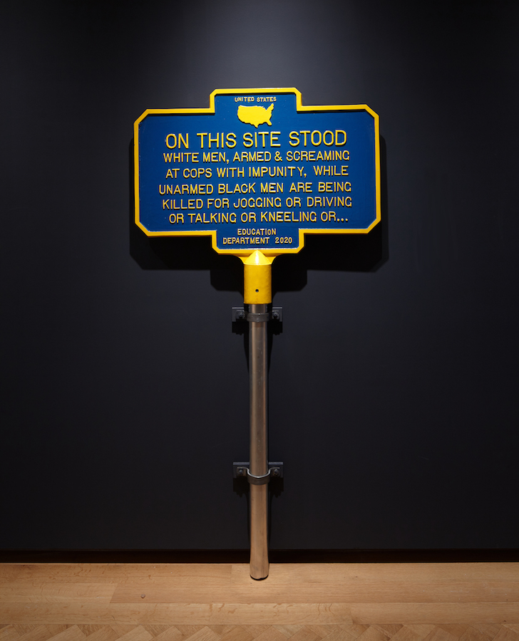 Blue and yellow metal sign in the style of historic landmark signs that marks the racial justice uprisings that took place during 2020.