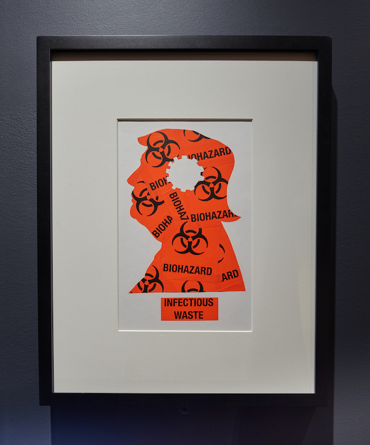 A matted, framed print that depicts a profile of Donald Trump created out orange biohazard labels.