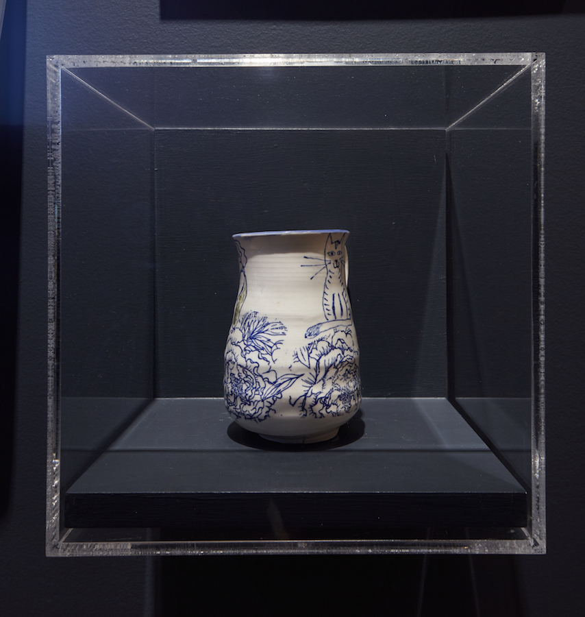 Taza de cerámica blanca con diseños florales azules. Un dibujo de un gato es visible en el lado derecho.