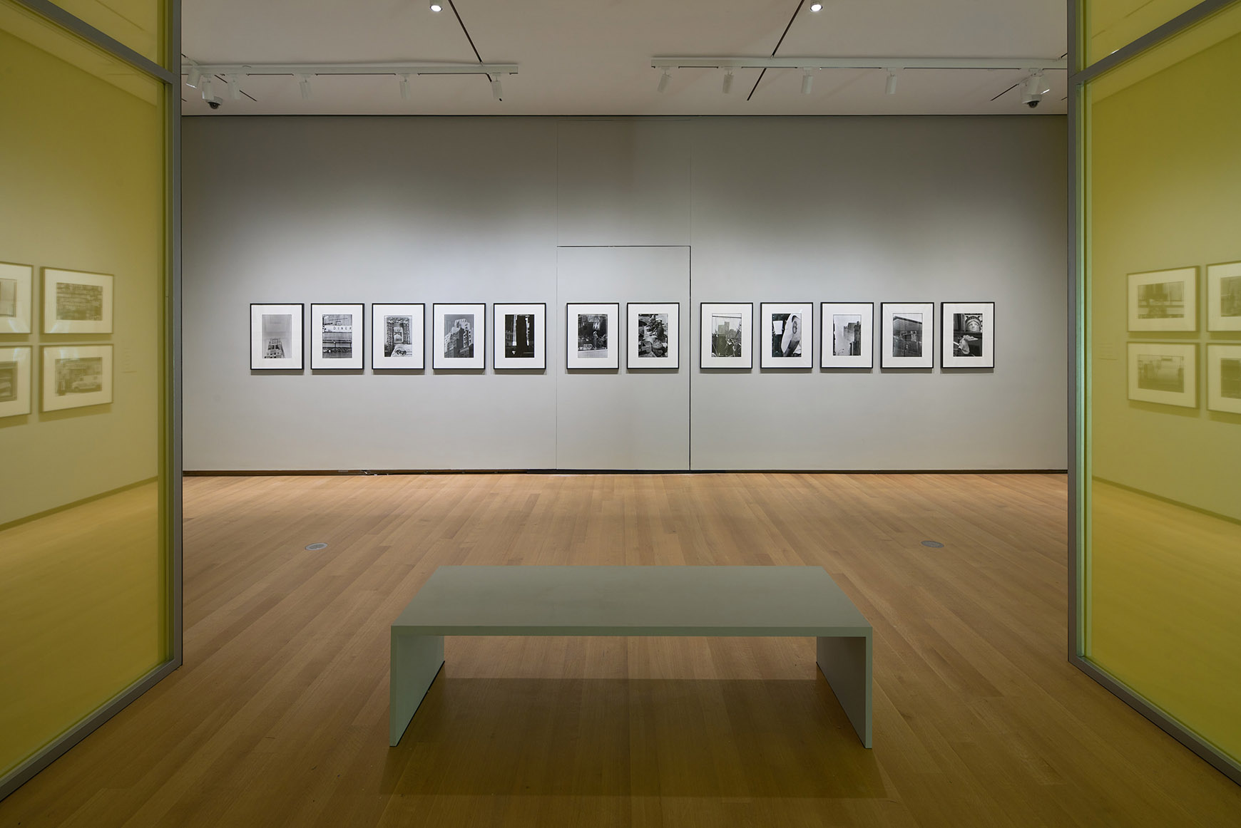 Installation of Robert Rauschenberg’s New York with a bench in front of a wall of photographs