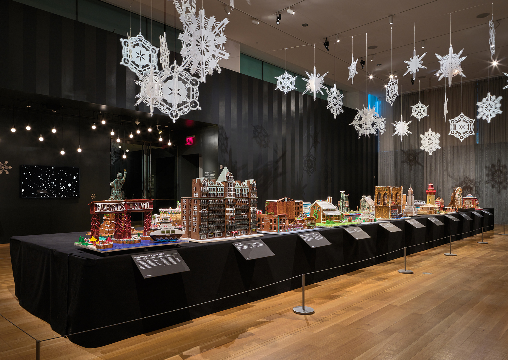 A long table with gingerbread houses inspired by New York, with lights and snowflakes hanging above