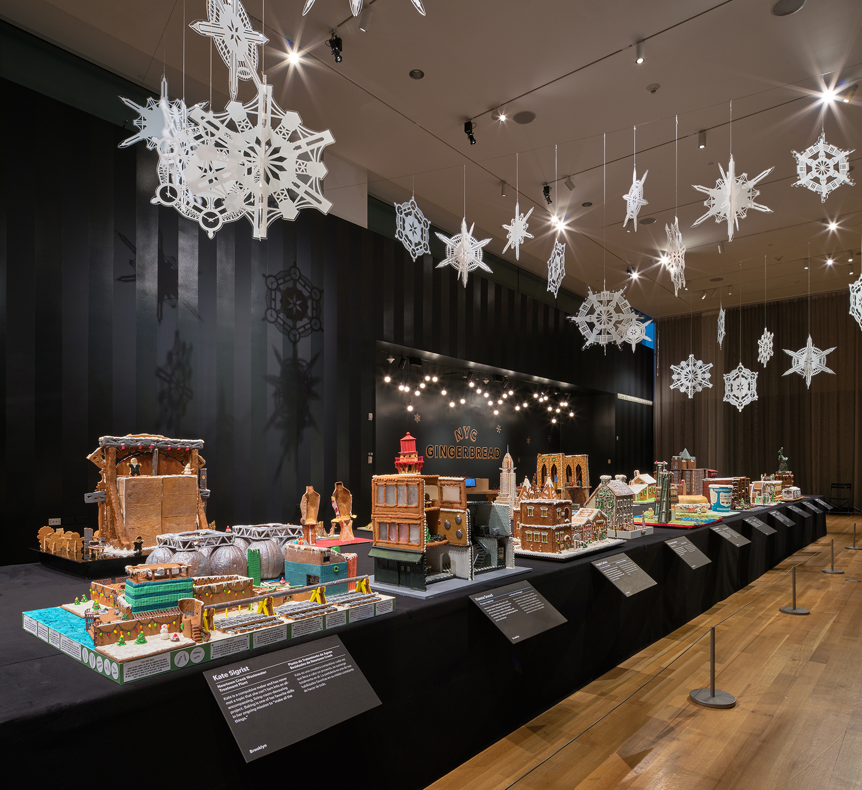 A long table with gingerbread houses inspired by New York, with lights and snowflakes hanging above