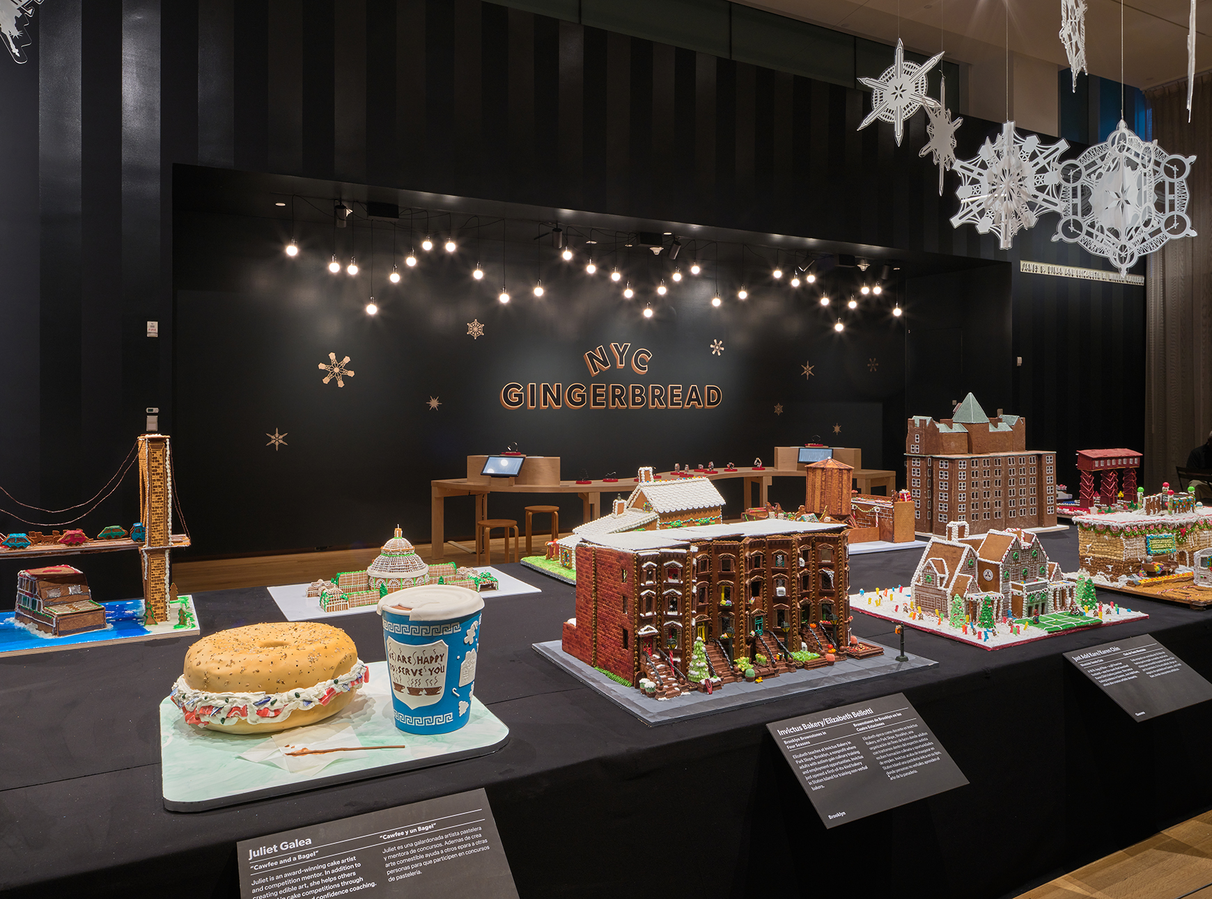 A long table with gingerbread houses inspired by New York, with lights and snowflakes hanging above