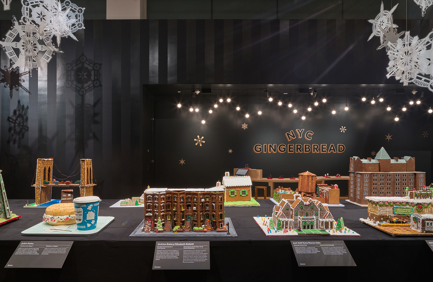 A long table with gingerbread houses inspired by New York, with lights and snowflakes hanging above