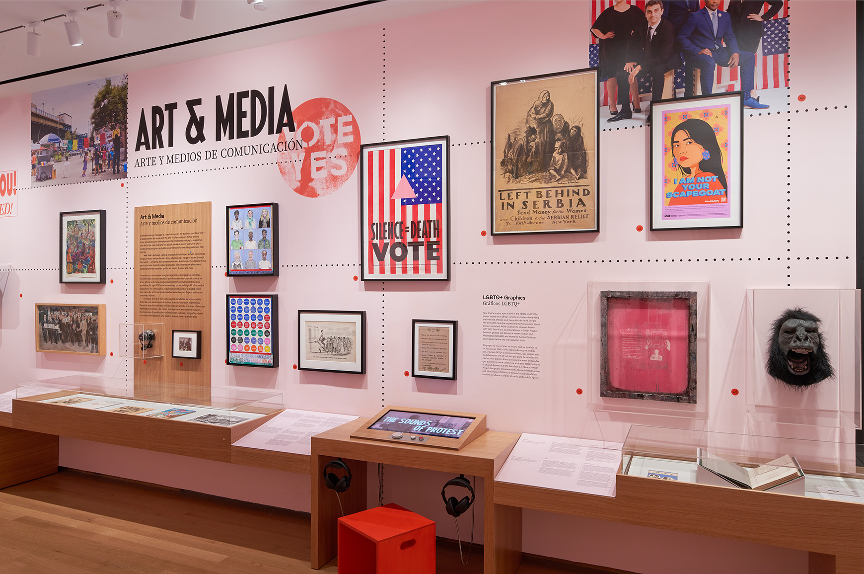 A gallery with pink walls and wooden cases showing photographs, sculptures, paintings, and interactive displays