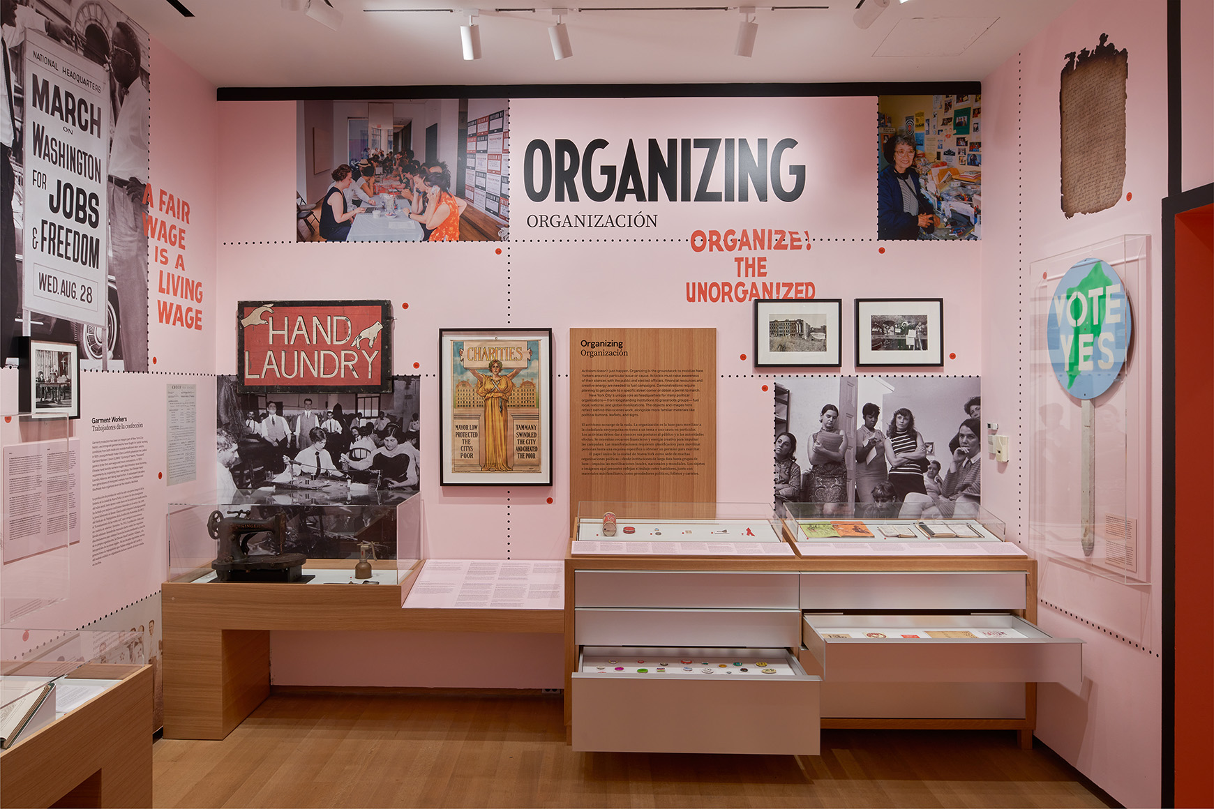 A gallery with pink walls and wooden cases showing photographs, sculptures, paintings, and interactive displays